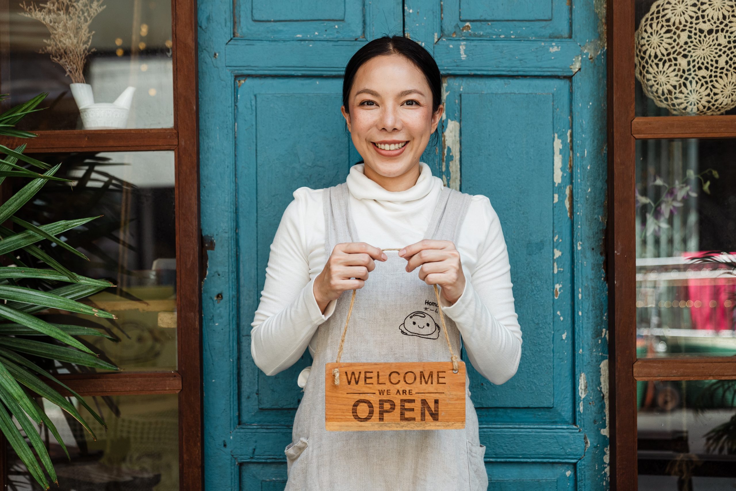 A small business owner holds up a sign saying "we are open" outside her store